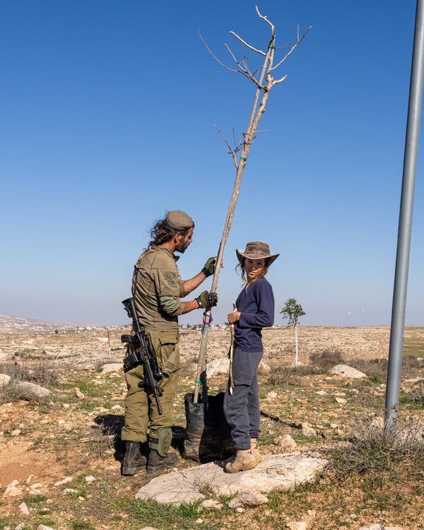 Someone in a uniform with a gun planting a tree with a young person in a weathered hat.