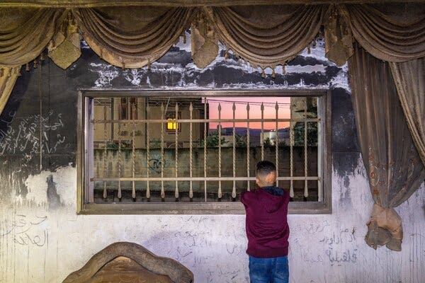 Ahmad Dawabsheh looking out a window to a village at dusk. He has a scar on the back of his head.